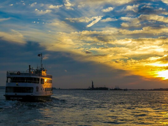 A ferry crossing the harbour toward Ellis Island at sunset, symbolising the hopes and uncertainties carried by those seeking a new beginning