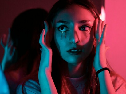 A woman holding her face as thoughts race inward, reflecting the exhausting cycle of self-judgment
