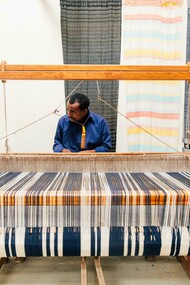 Tecelão artesanal. A produção artesanal é, por natureza, mais lenta e limitada em quantidade, o que reduz a pressão sobre os recursos naturais. Esta abordagem slow fashion contrasta fortemente com a mentalidade de fast fashion, incentivando os consumidores a valorizar mais cada peça de roupa, em vez de comprar e descartar rapidamente. É um convite à reflexão sobre o verdadeiro valor das roupas e a história que cada fio carrega
