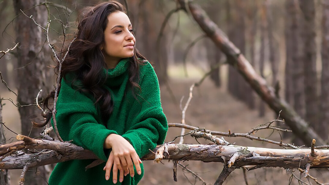 Woman in nature enjoying view, leaning on the tree branch