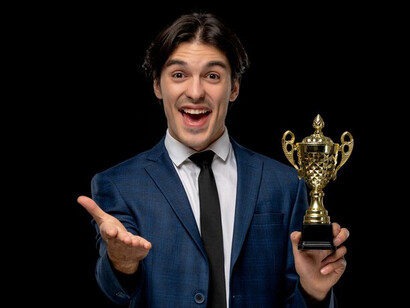 A young, excited, and handsome businessman in a dark blue suit and tie, holding a trophy, celebrating success