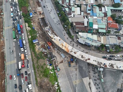 Vehicles trapped beside a massive unfinished infrastructure project, representing the gap between ambitious development and everyday public realities