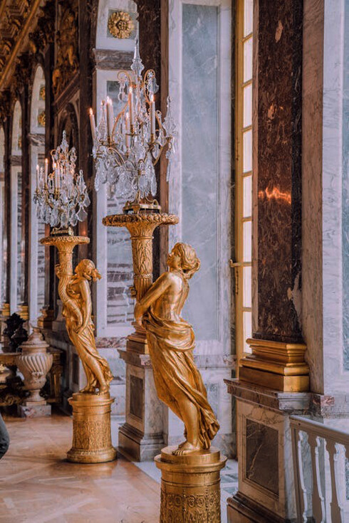 A golden statue holding a candle holder stands gracefully in the opulent Palace of Versailles, reflecting the grandeur of its royal history, France