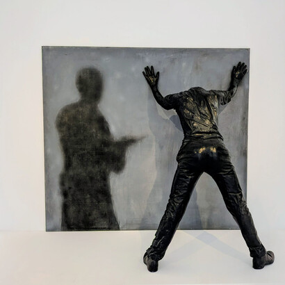 Rafael Canogar (b. 1935). The artwork in the image is titled El Arresto II (The Arrest II) (1972). Canogar is a significant Spanish artist known for co-founding the El Paso group and for his work in both informal abstraction and figurative art with socio-political themes, such as police brutality. This piece is from Canogar's second figurative period. It breaks the barrier between painting and sculpture to create a 3D effect, focusing on themes of dehumanization, repression, and social critique. The sculpture of the figure against the wall with hands up is depicted alongside a painted shadow figure holding what appears to be a gun. Image ©MACA/the Author 2026