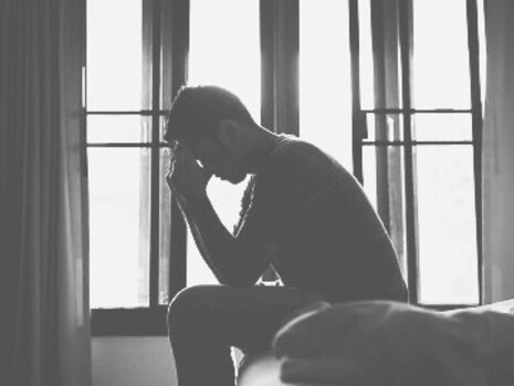 A man overthinking sitting on his bed. Men are socialized to communicate ‘rationally’ and without ‘feelings'