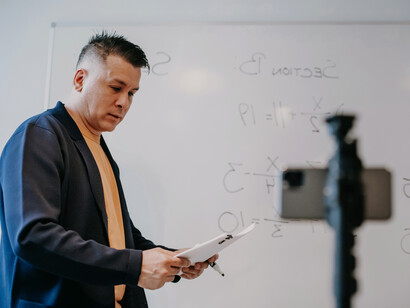 Professor olha para o rascunho enquanto transmite uma aula para seus alunos que o assistem de casa