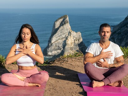 A man and woman practicing slow, mindful breathing in a peaceful coastal setting, symbolizing the connection between breath and emotional balance