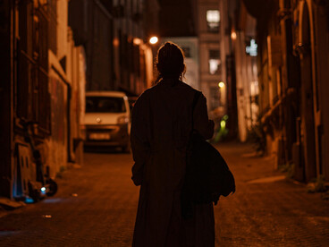 Silhouettes of men on a narrow road, with figures walking along a dark, foggy pavement