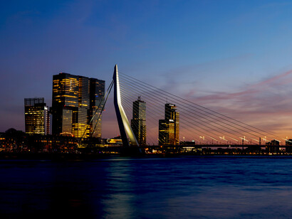 Blue hour in Rotterdam, Netherlands, featuring a bridge stretching over calm water with the city skyline illuminated in the background