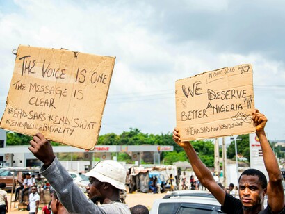 Citizens holding protest signs during a public demonstration, reflecting public dissatisfaction with political and social conditions