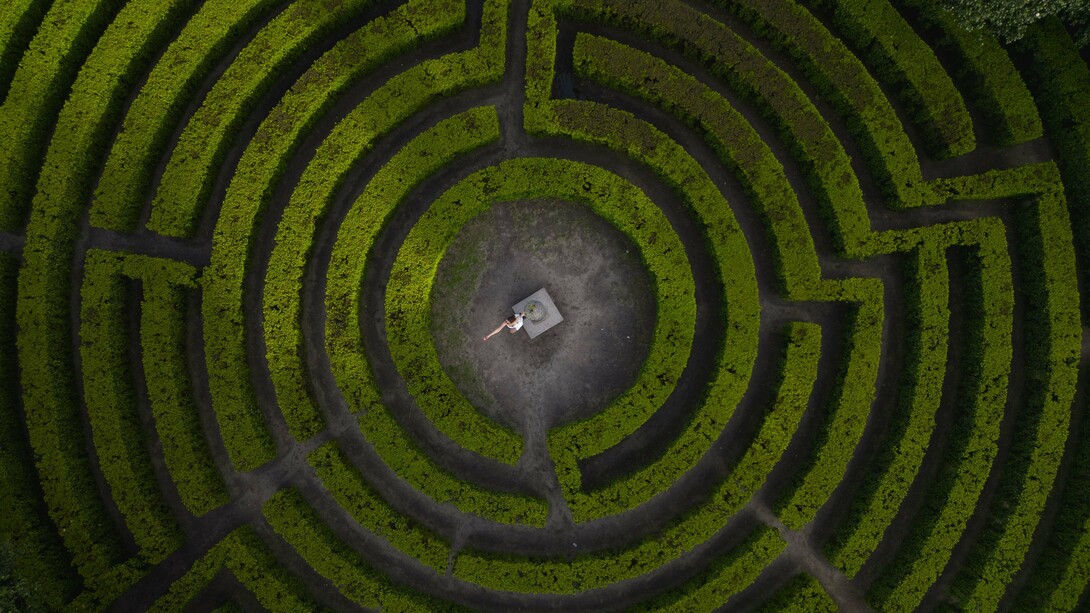 A person standing at the heart of a vast maze, symbolizing humanity’s struggle to maintain direction during times of uncertainty