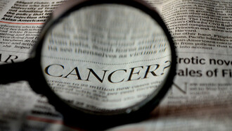 Beneath the magnifying glass, the word 'cancer' becomes apparent on the newspaper