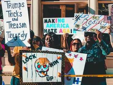 Protesters holding signs condemning Trump and calling for America to change course, reflecting collective resistance to the turmoil and uncertainty of the Trump era