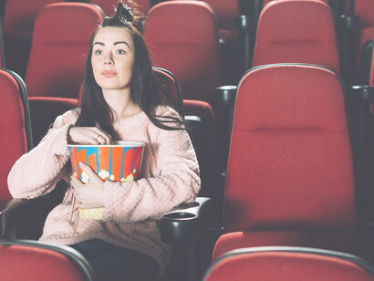 A brunette woman eating popcorn in a movie theater, embracing the full cinematic experience