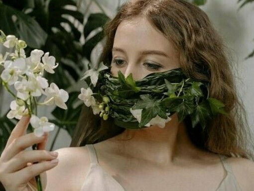 A woman staring quietly through layers of leaves and flowers, representing the internal tension between visibility and silence