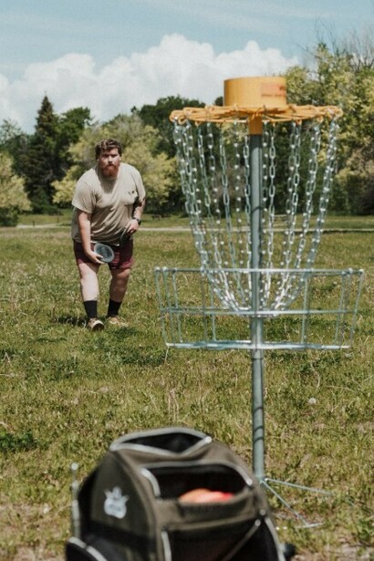 A man throwing a disc toward a disc golf basket