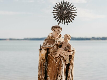 A imagem mostra uma representação de Santo Antônio diante do mar, com o Menino Jesus nos braços e uma auréola em destaque. A figura do santo, tradicionalmente associada à devoção popular e aos pedidos por casamento, ocupa papel central na narrativa de Socorro Acioli