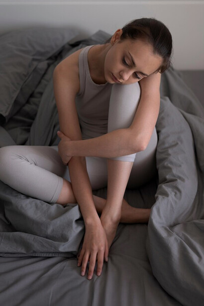 A depressed woman sitting on the bed wrapped in a blanket, illustrating the emotional challenges and isolation often experienced in mental health struggles