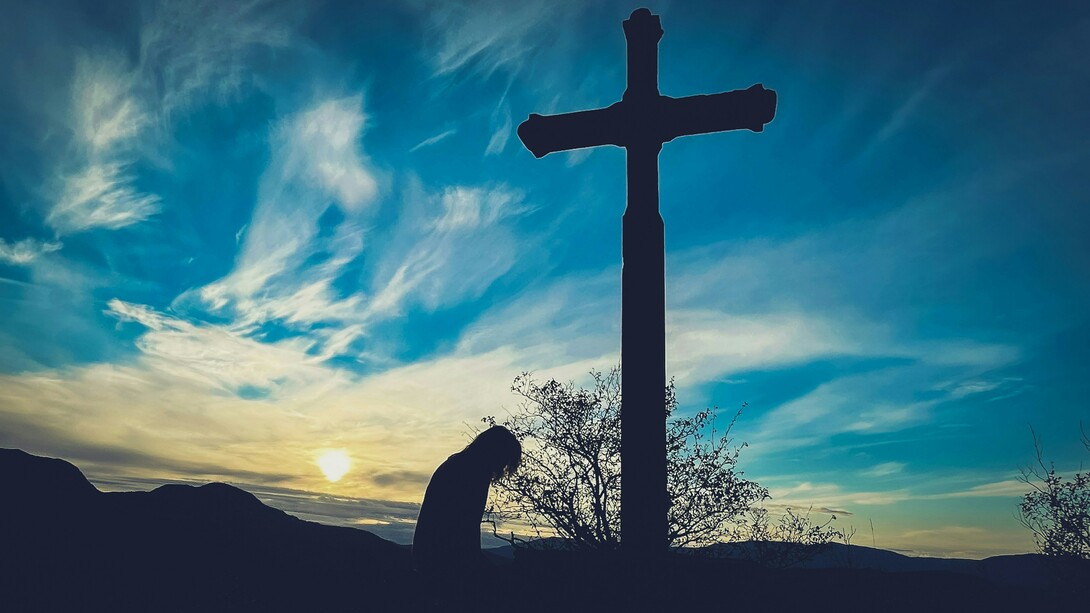 A person kneeling before a cross on a hill, representing a return to sincere and humble faith
