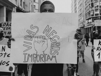 Homem participa de manifestação segurando um cartaz com a frase "Vidas negras importam". A luta contra o racismo aparece no texto como parte inseparável de qualquer projeto emancipatório
