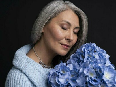 A woman with elegant silver hair holding a bunch of flowers, reflecting the confidence that can grow alongside natural aging
