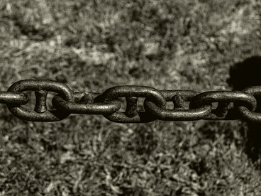 Heavy iron chains stretched across the ground evoke the physical restraint of enslaved labor, a system that generated wealth while enforcing total control over Black bodies