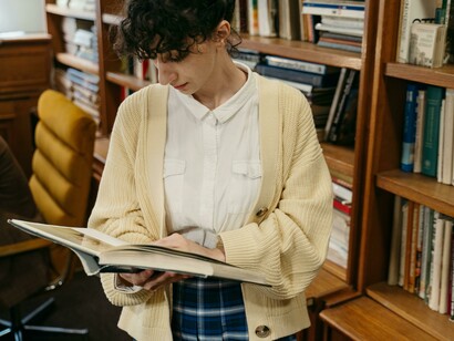 A woman wearing a knitted cardigan quietly reads a book in the library