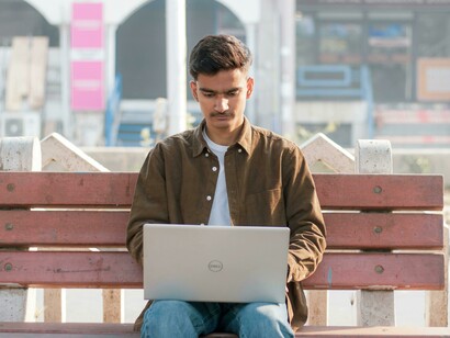 In a quiet park, a young Indian man searches for job opportunities on his laptop
