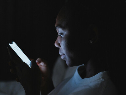 Woman illuminated by screens while using her phone in a dark room at night