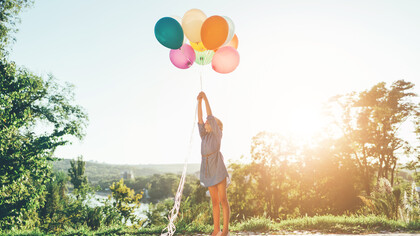 A girl reaches out toward colorful balloons, smiling with pure happiness