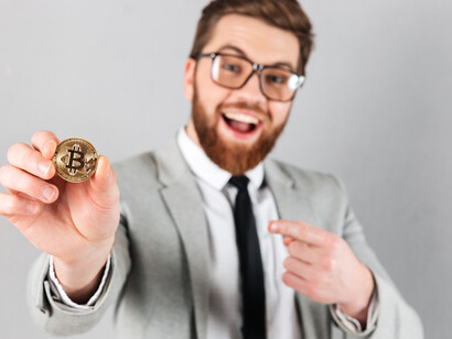 A smiling businessman dressed in a suit holding a bitcoin, highlighting the rise of digital currency