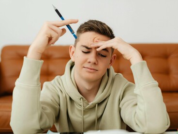 Um estudante encara os livros com expressão de dificuldade diante do conteúdo. É no desconforto do aprendizado que se desenvolvem a persistência e a capacidade de superar limites
