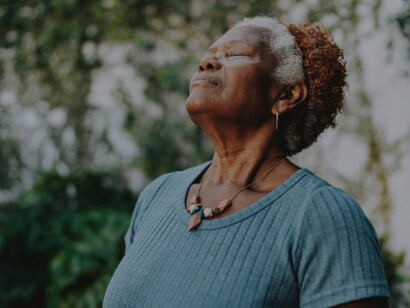 A senior lady practicing mindful breathing among lush forest trees, promoting relaxation and well-being