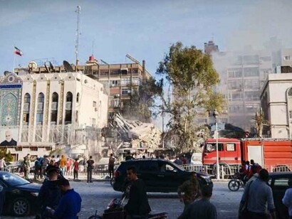 O local do ataque ao complexo diplomático iraniano aparece integrado à paisagem urbana de Damasco, com bombeiros, veículos de emergência e moradores diante dos escombros. A destruição de uma instalação vinculada ao Irã em território sírio tornou-se um dos episódios emblemáticos da escalada da rivalidade entre Teerã e Tel Aviv e Washington