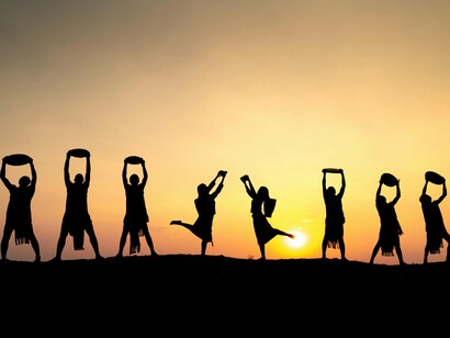 Silhouettes of a group of people holding objects high against a sunset backdrop, symbolizing unity and collective strength, and how working together as a team enhances focus, boosts productivity, and provides the social interaction necessary to prevent the isolation that can negatively impact both work performance and mental well-being
