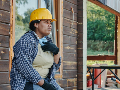 A woman wearing a yellow hard hat and a black-and-white plaid shirt works diligently to earn a living