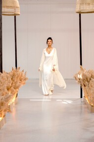 Uma modelo usando um vestido branco andando na passarela