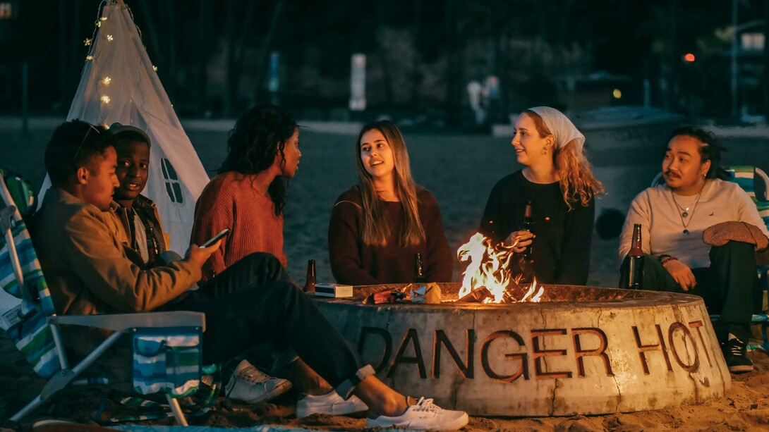 A group of friends sits around a fire pit, sharing stories in a circle during a community storytelling event