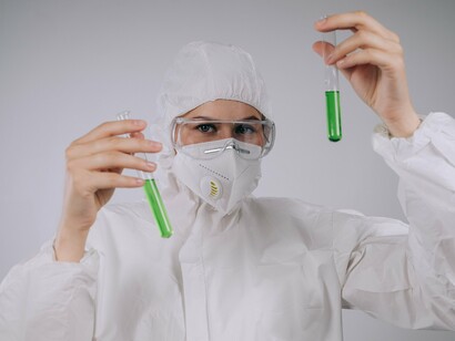 Profissional equipada para trabalhar em laboratório segura tubos de ensaio com amostras durante um experimento. A fotografia remete aos procedimentos utilizados para analisar a composição e a segurança de diferentes produtos