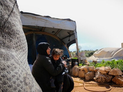 A mother in a headscarf cradles her baby in Idlib Governorate, Syria