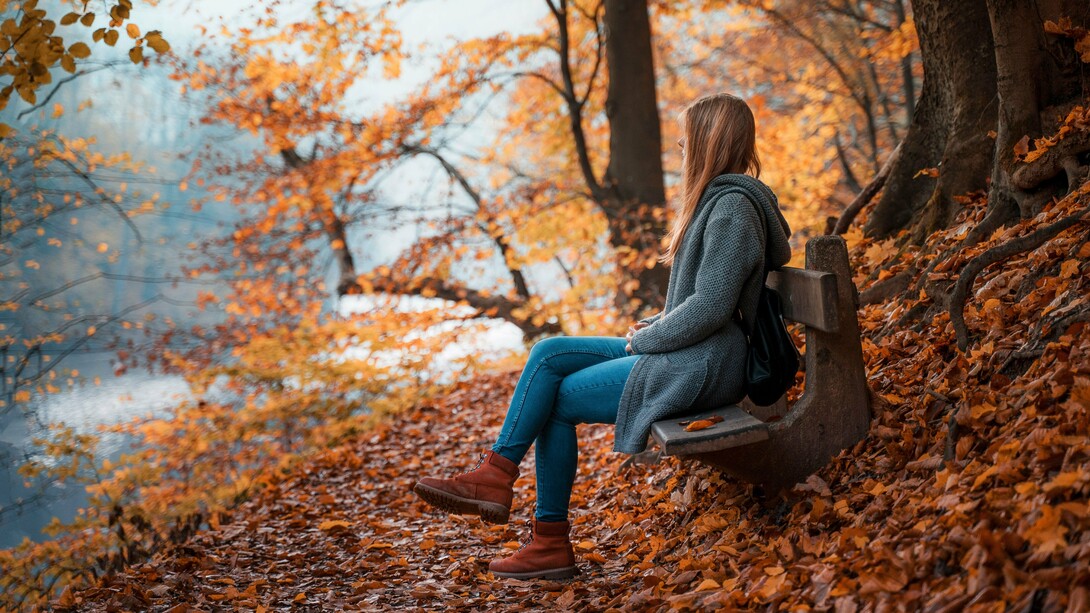 A woman sitting quietly on a bench surrounded by autumn leaves, representing the beauty of embracing a slower, simpler life