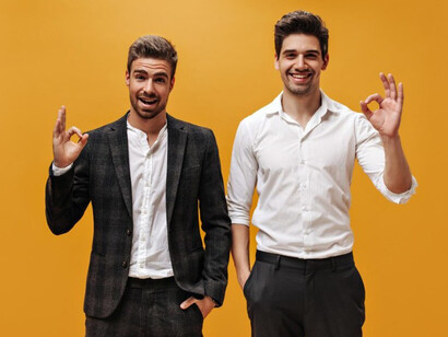 Confident and happy young men in traditional business attire celebrate their achievements on a bold orange background