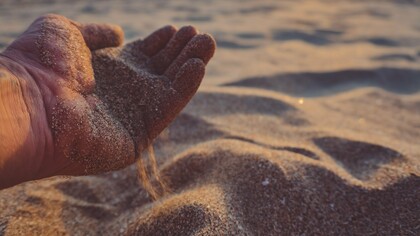 A hand pouring sand out, reflecting how peace sometimes requires us to loosen our grip on old troubles