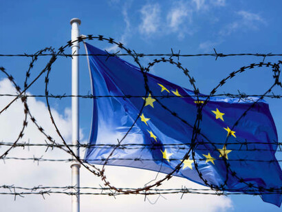 The EU flag flutters in the overcast sky above the prison’s barbed wire, standing as a quiet emblem of border enforcement