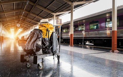 Bagagens aguardam ao lado de um trem em uma estação iluminada pelos primeiros raios de sol. A imagem representa o momento concreto da partida, enquanto a ansiedade pré-viagem muitas vezes começa muito antes, ainda no espaço íntimo de casa