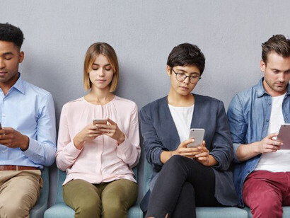 A group of people sit in a waiting room, absorbed in their phones