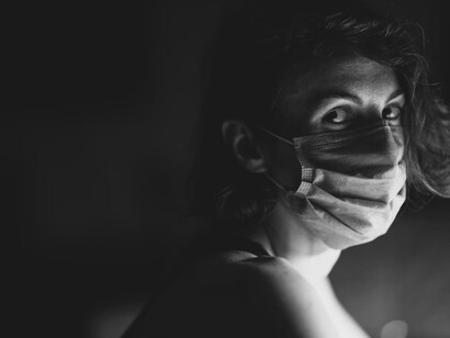 A person with their head down on a desk, wearing a mask
