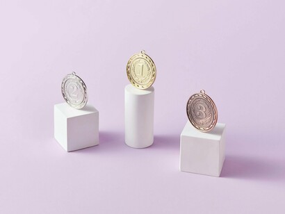 Three medals in gold, silver, and bronze showcased on stands, reflecting the system of constant evaluation and comparison