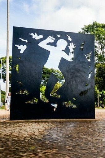 Detalhes da escultura do artista plástico goiano Siron Franco destacam a força simbólica da homenagem. A presença do memorial contrasta com a liberdade dos responsáveis, levantando reflexões sobre justiça moral