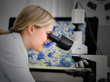 Female scientist using a microscope in a modern biomedical engineering research laboratory